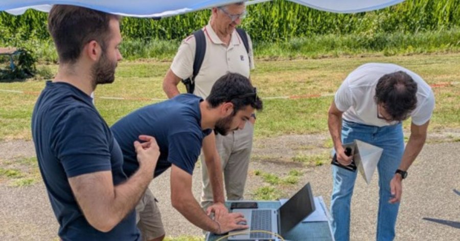 Tre uomini in piedi attorno a un tavolo con laptop aperti, discutendo e collaborando su un progetto.