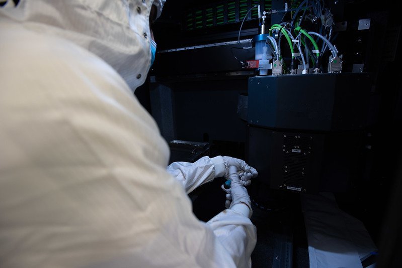 A PhD candidate is working with a inkjet-aerosol jet printer installed in the clean room of Polifab.