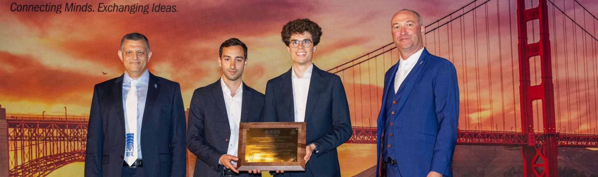 Tre uomini in giacca e cravatta tengono un premio davanti a una riproduzione del Golden Gate Bridge. Tre uomini in giacca e cravatta tengono un premio davanti a una riproduzione del Golden Gate Bridge.
