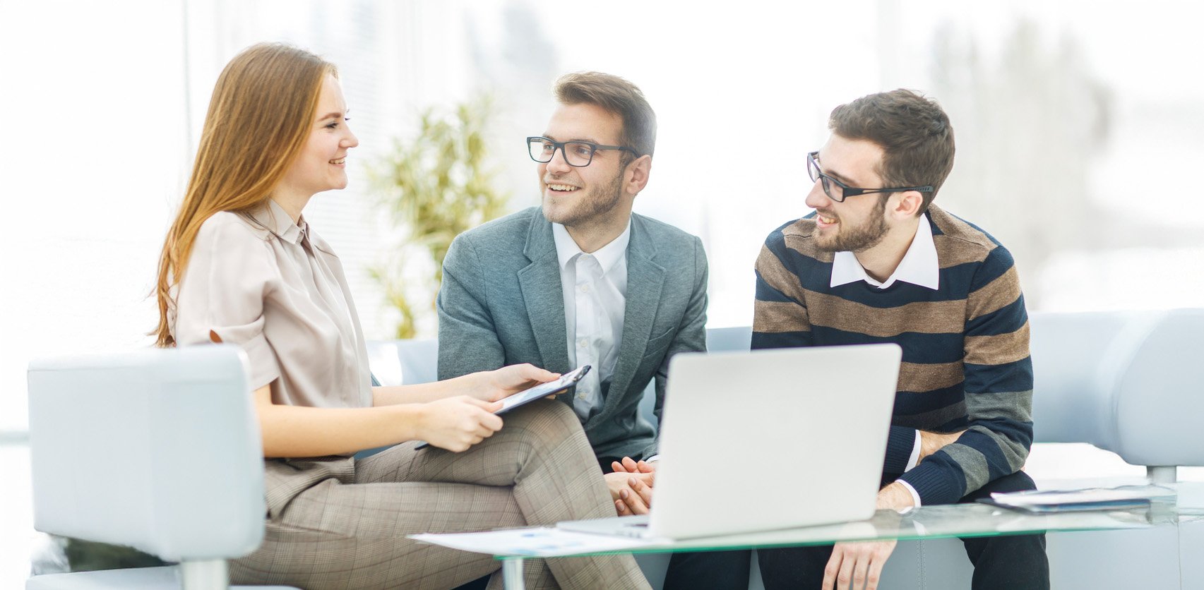 Three people sitting around a laptop, talking and collaborating on a project.