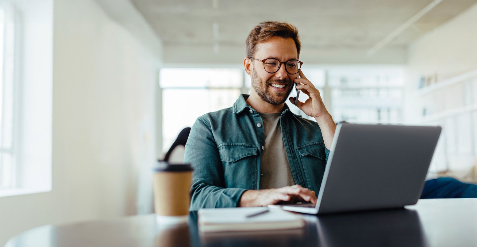 Un uomo con occhiali e laptop parla al telefono, concentrato sul suo lavoro.