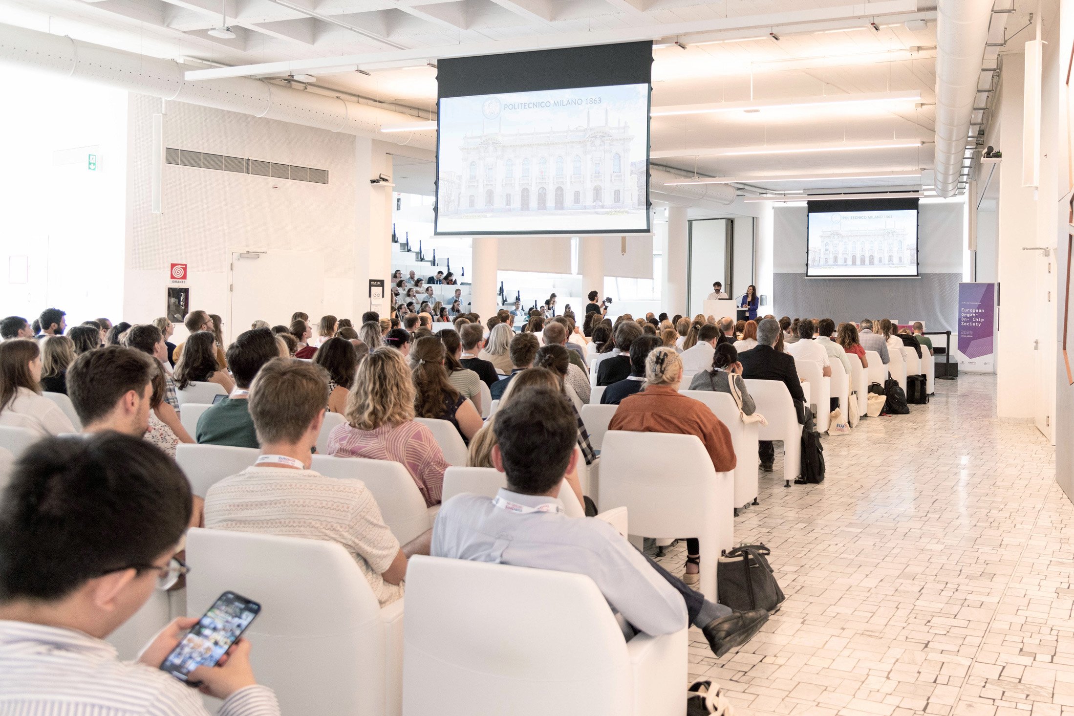 A large group of people sitting on chairs in a room, all facing a speaker or an ongoing event.